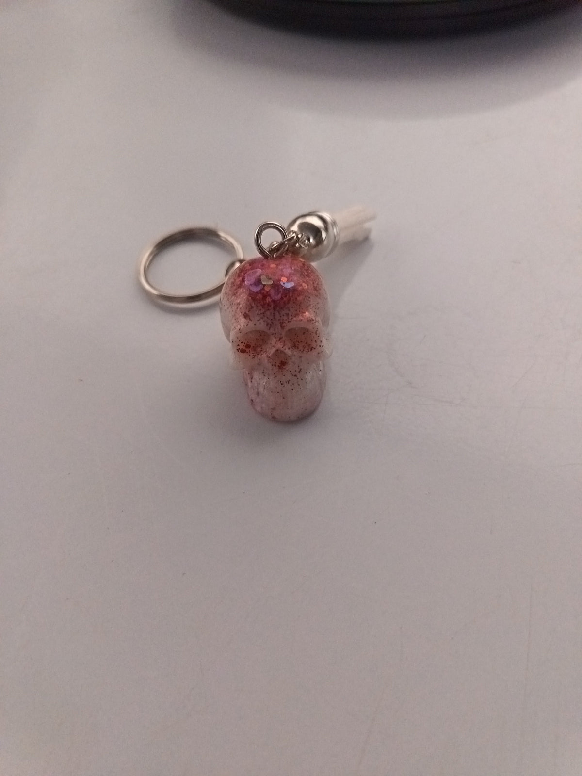 Porte-clé tête de mort sculptée en résine rose translucide avec grosses paillettes roses