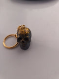 Porte-clé tête de mort sculptée en résine noire avec paillettes dorées et anneau doré