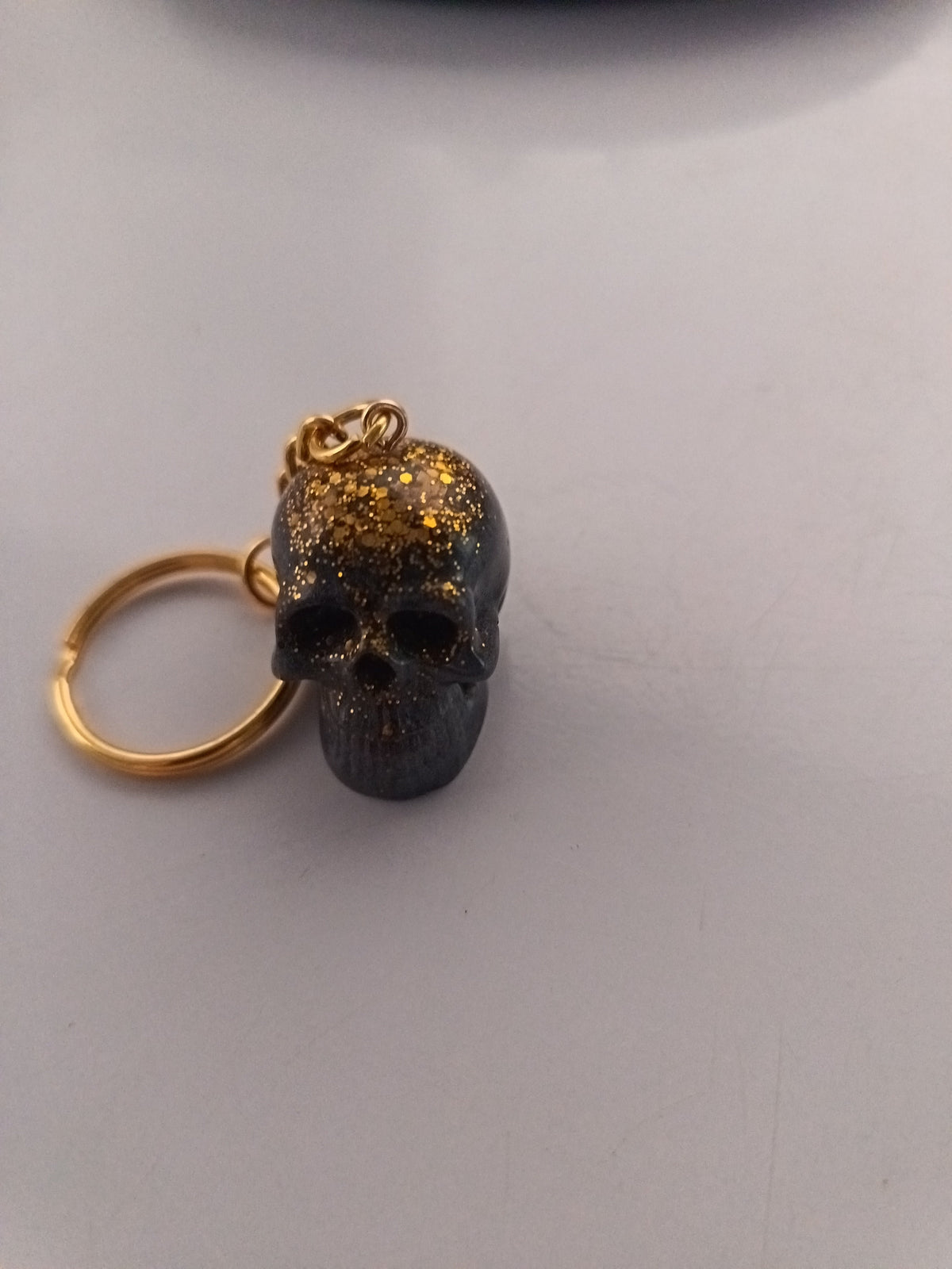 Porte-clé tête de mort sculptée en résine noire avec paillettes dorées et anneau doré