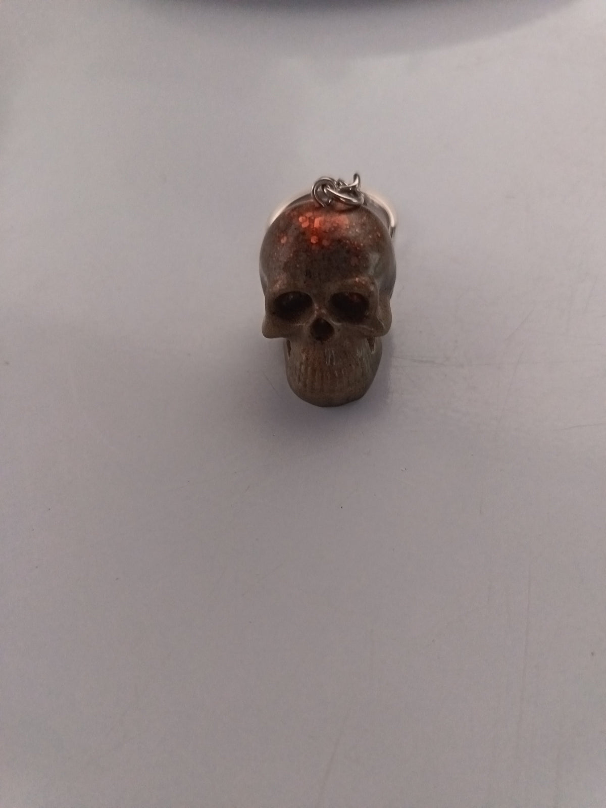 Porte-clé tête de mort sculptée en résine beige-taupe avec paillettes oranges-cuivrées