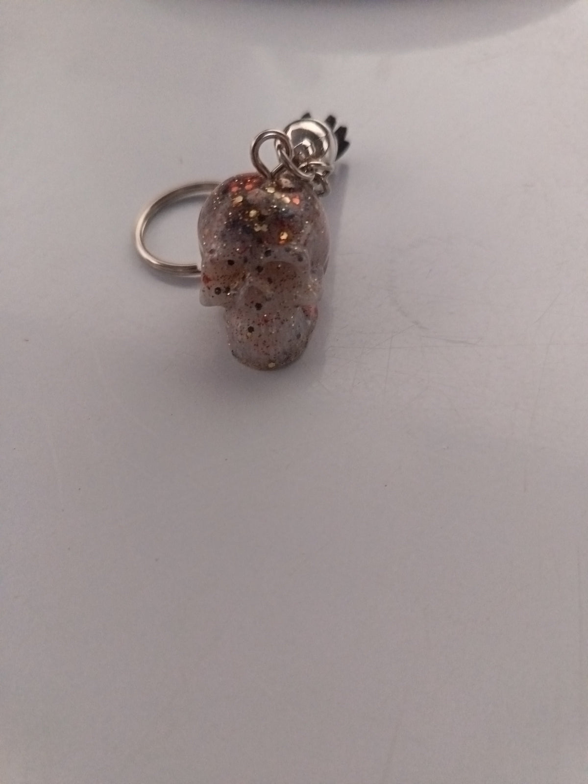 Porte-clé tête de mort en résine translucide rosée avec paillettes dorées et breloque couronne argentée