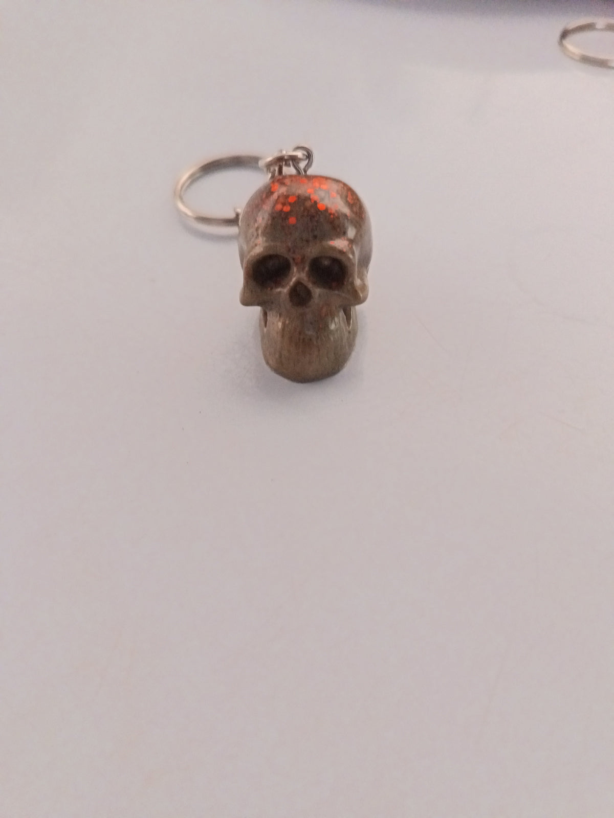 Porte-clé tête de mort sculptée en résine bronze-brun avec paillettes oranges-rouges