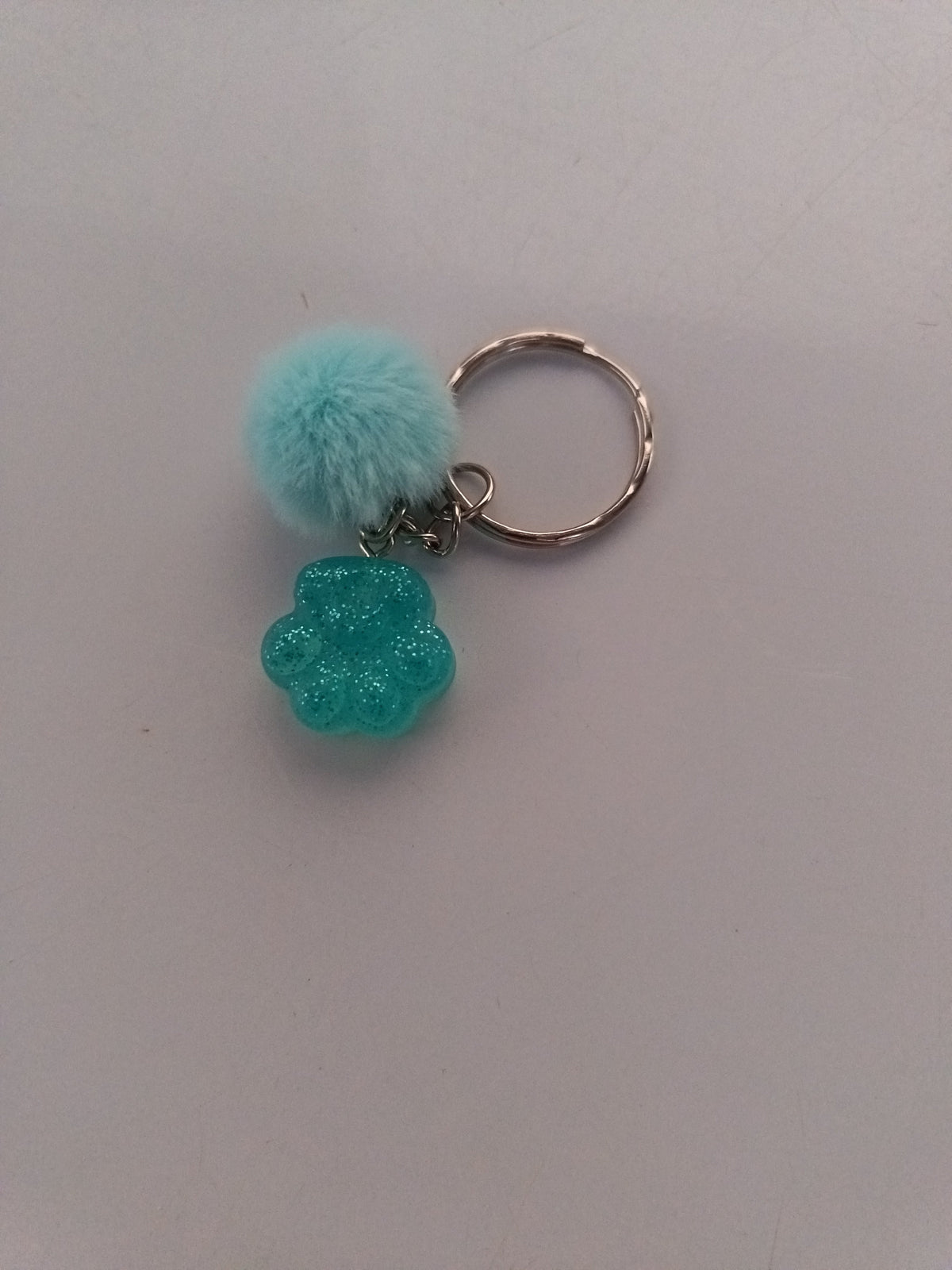 Porte-clé patte de chien sculptée en résine turquoise pailletée avec pompon fourrure turquoise
