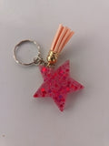 Porte-clé étoile en résine fuchsia à grosses paillettes rondes avec pompon suédine pêche et breloque dorée
