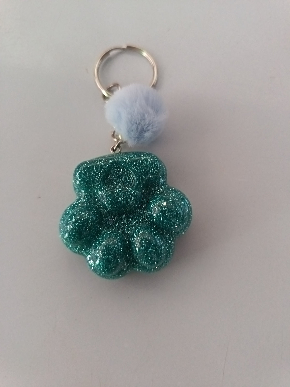 Porte-clé grosse patte de chien sculptée en résine vert émeraude pailleté avec pompon boule de fourrure bleu ciel