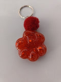 Porte-clé grosse patte de chien en résine rouge translucide à grosses paillettes avec pompon boule rouge bordeaux