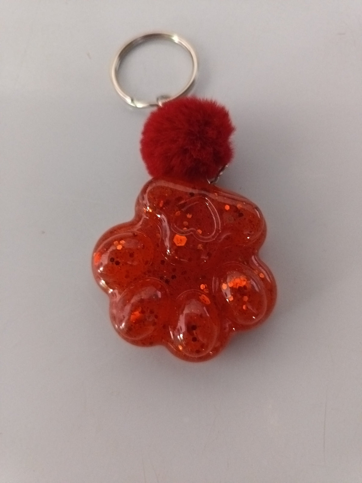 Porte-clé grosse patte de chien en résine rouge translucide à grosses paillettes avec pompon boule rouge bordeaux