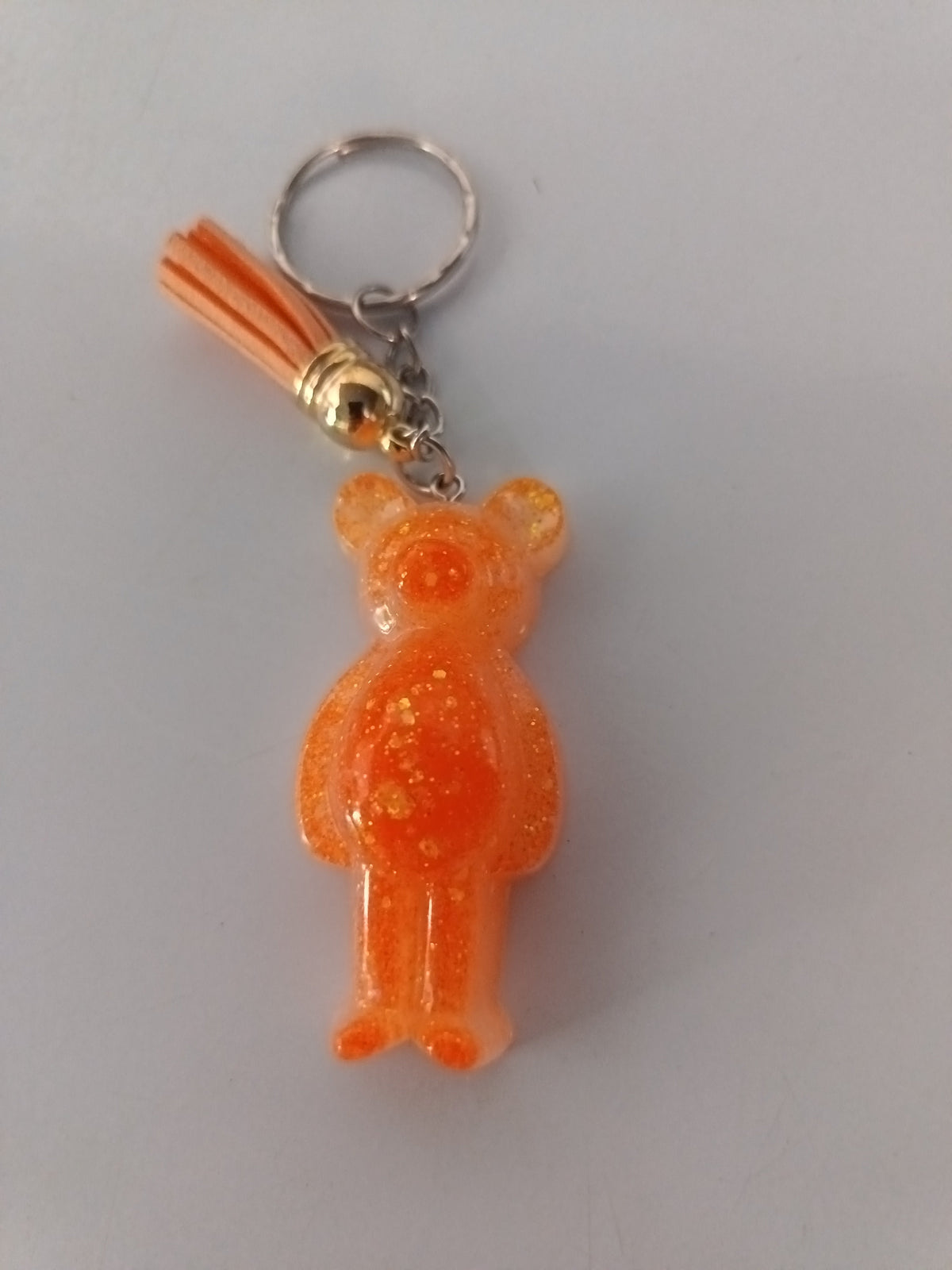 Porte-clé ourson sculpté en résine orange translucide pailleté avec pompon suédine orange et chaînette argentée
