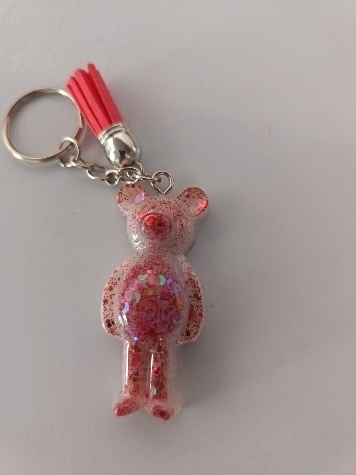 Porte-clé ourson sculpté en résine rose translucide à grosses paillettes irisées avec pompon suédine rouge corail