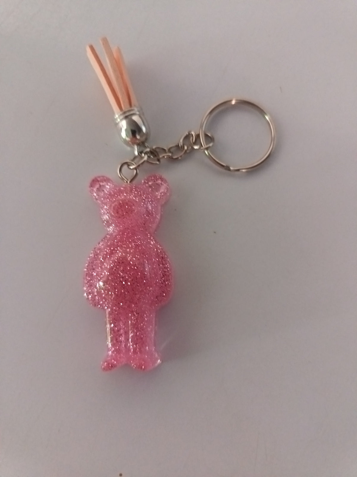 Porte-clé ourson sculpté en résine rose translucide ultra-pailleté avec pompon suédine pêche et chaînette argentée