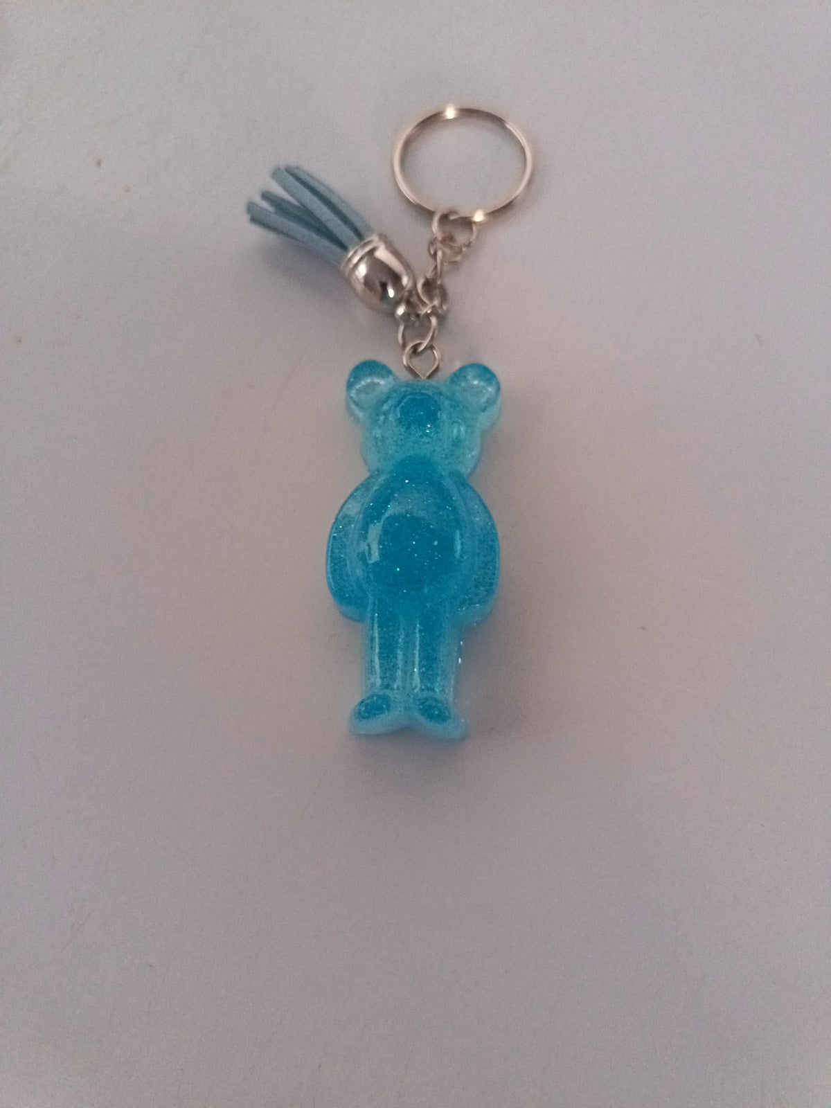 Porte-clé ourson sculpté en résine bleu ciel translucide pailleté avec pompon suédine bleu ciel
