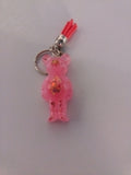 Porte-clé ourson sculpté en résine rose translucide à grosses paillettes holographiques avec pompon suédine rouge vif