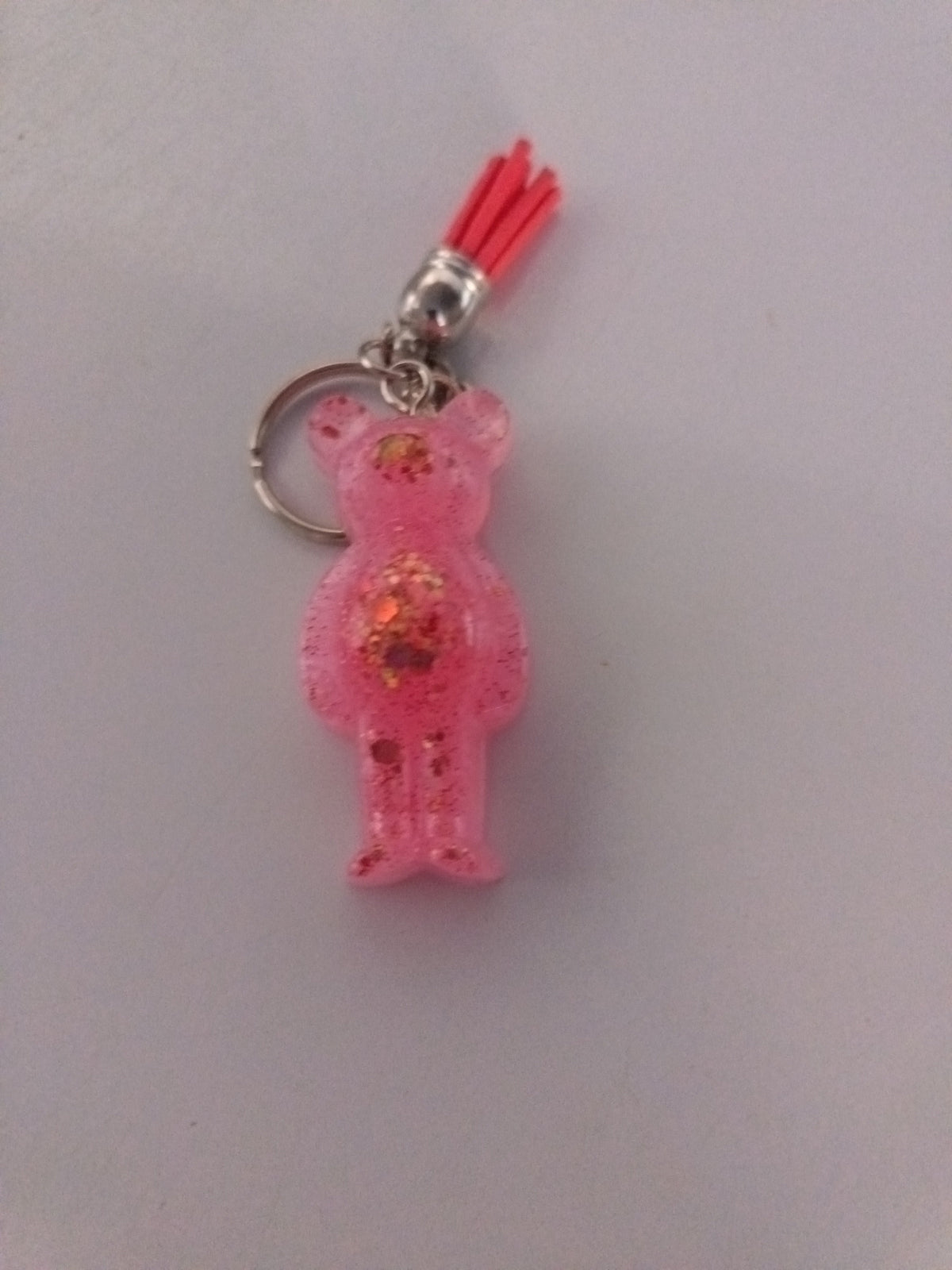 Porte-clé ourson sculpté en résine rose translucide à grosses paillettes holographiques avec pompon suédine rouge vif