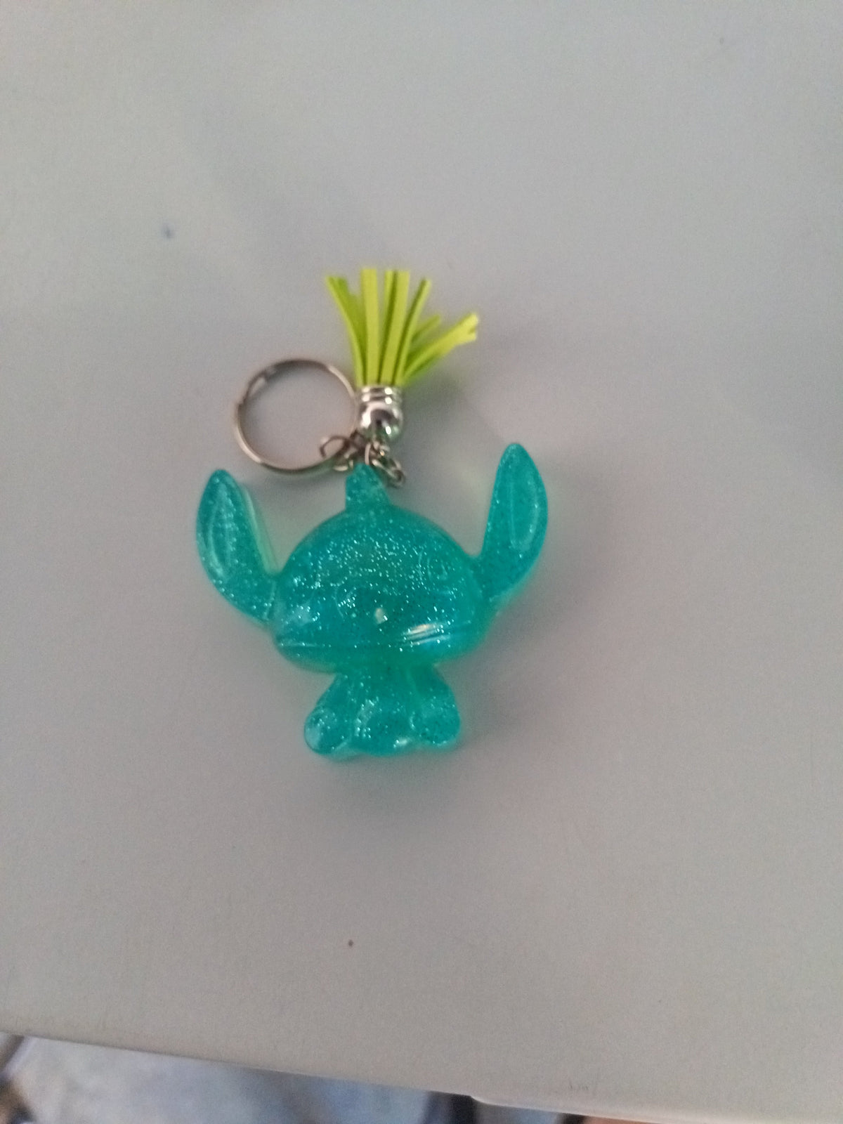 Porte-clé Stitch sculpté en résine turquoise pailleté avec pompon suédine jaune fluo