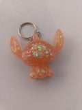 Porte-clé Stitch sculpté en résine pêche-abricot translucide à grosses paillettes holographiques irisées