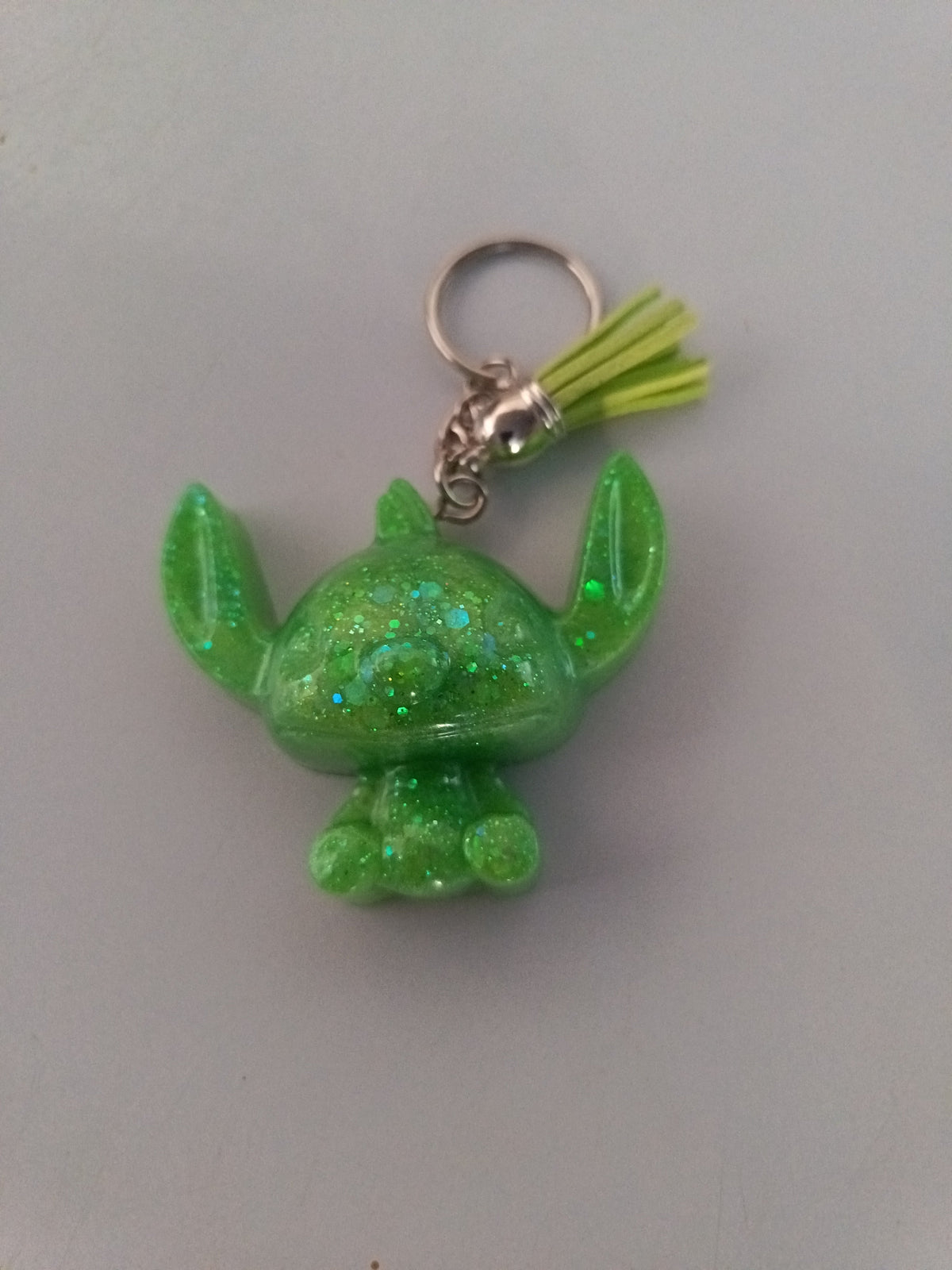 Porte-clé Stitch sculpté en résine vert fluo translucide à grosses paillettes holographiques avec pompon suédine jaune anis