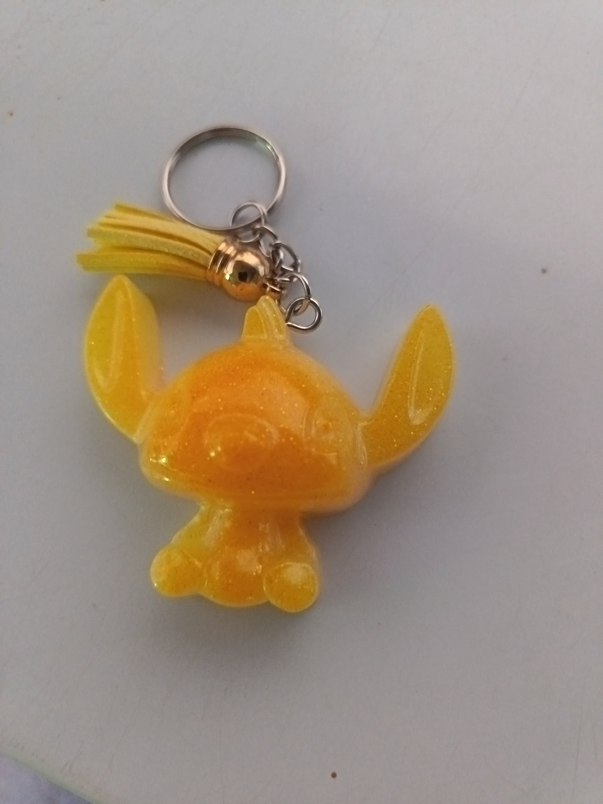 Porte-clé Stitch sculpté en résine jaune doré translucide pailleté avec pompon suédine jaune et breloque dorée
