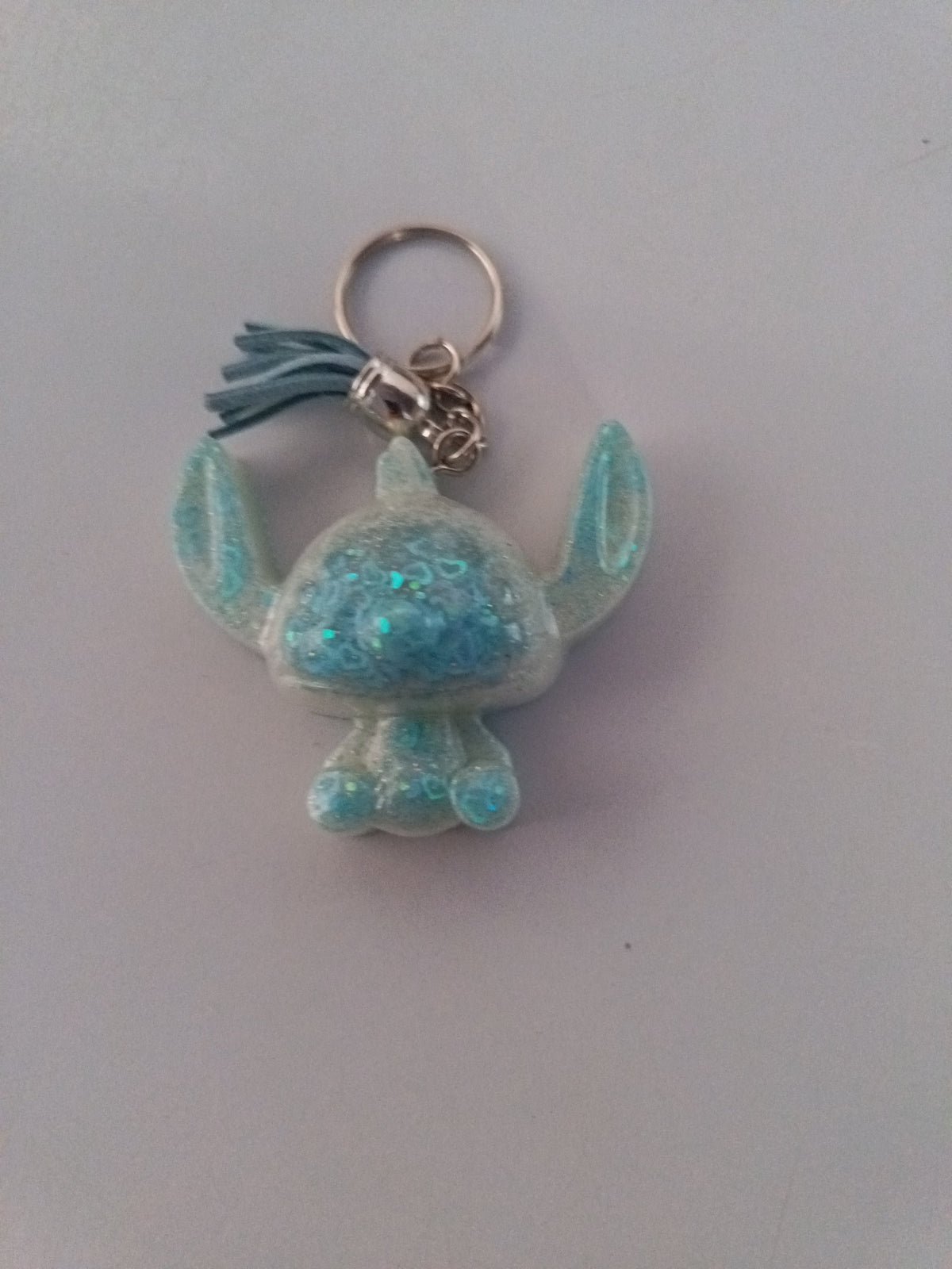Porte-clé Stitch sculpté en résine blanc nacré translucide à grosses paillettes turquoise avec pompon suédine bleu ciel