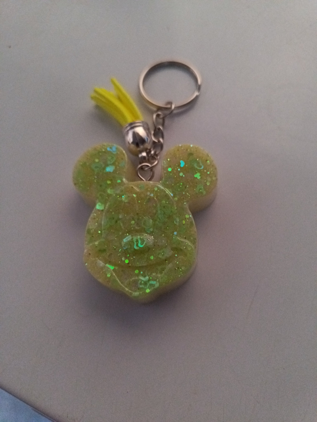 Porte-clé tête de Mickey sculptée en résine vert anis translucide à grosses paillettes holographiques avec pompon suédine jaune fluo