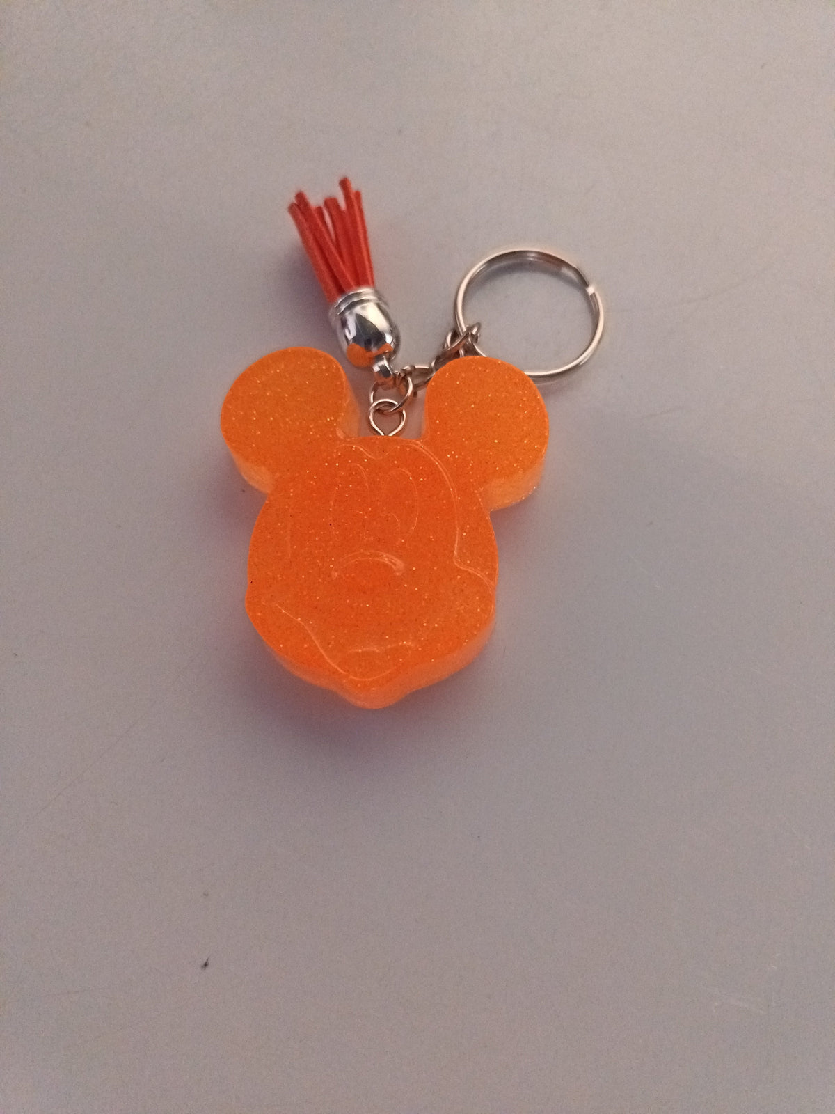 Porte-clé tête de Mickey sculptée en résine orange vif translucide à micro-paillettes avec pompon suédine rouge