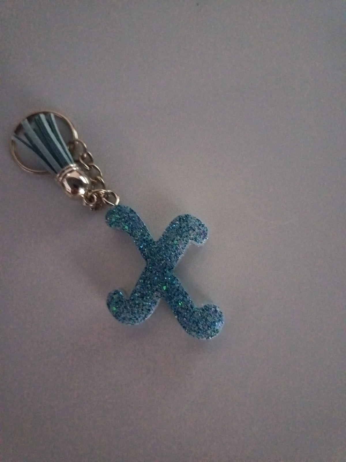 Porte-clé lettre X sculptée en résine bleu ciel ultra-pailleté avec pompon suédine bleu et clip mousqueton argenté