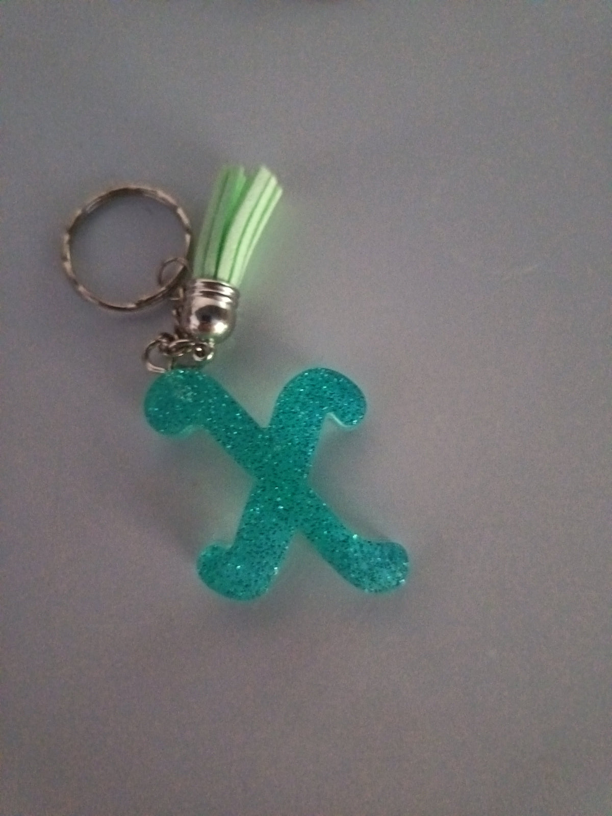 Porte-clé lettre X sculptée en résine turquoise ultra-pailleté avec pompon suédine vert menthe et chaînette argentée