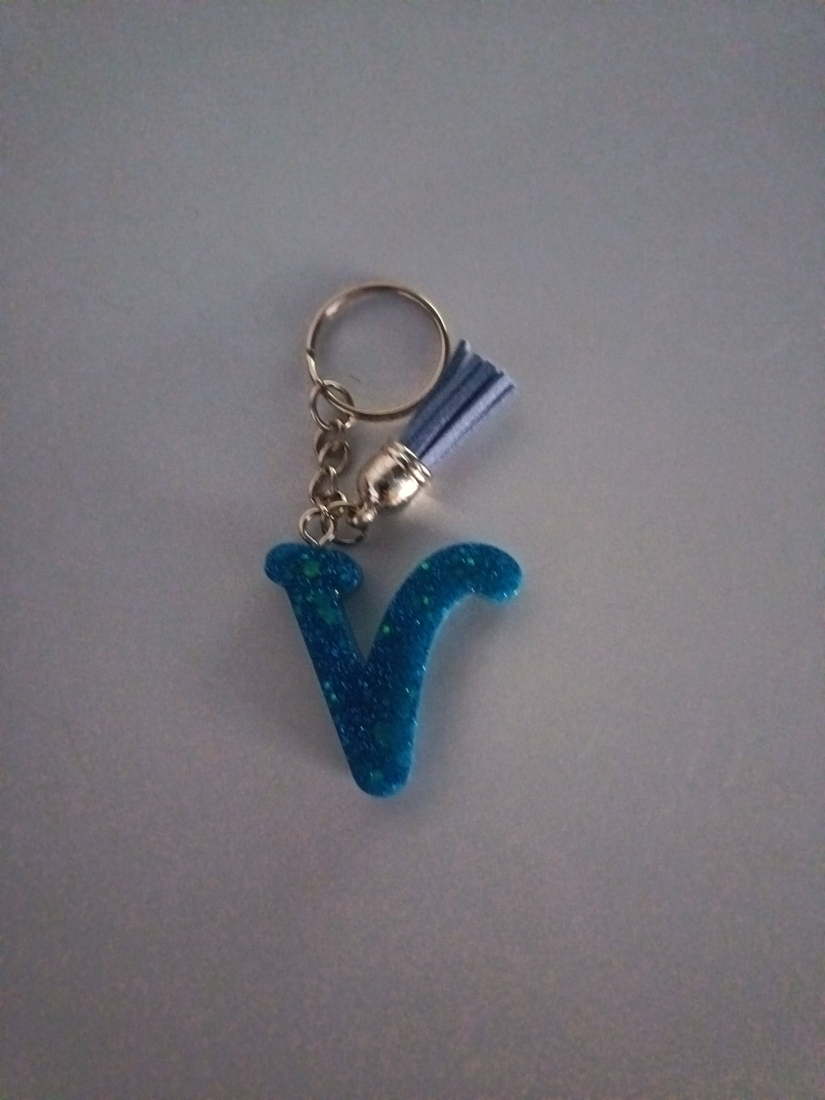 Porte-clé lettre V sculptée en résine bleu turquoise ultra-pailleté avec pompon suédine bleu lavande et chaînette argentée