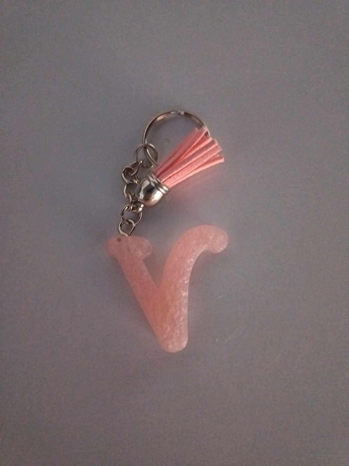 Porte-clé lettre V sculptée en résine rose poudré nacré avec pompon suédine rose saumon et chaînette argentée
