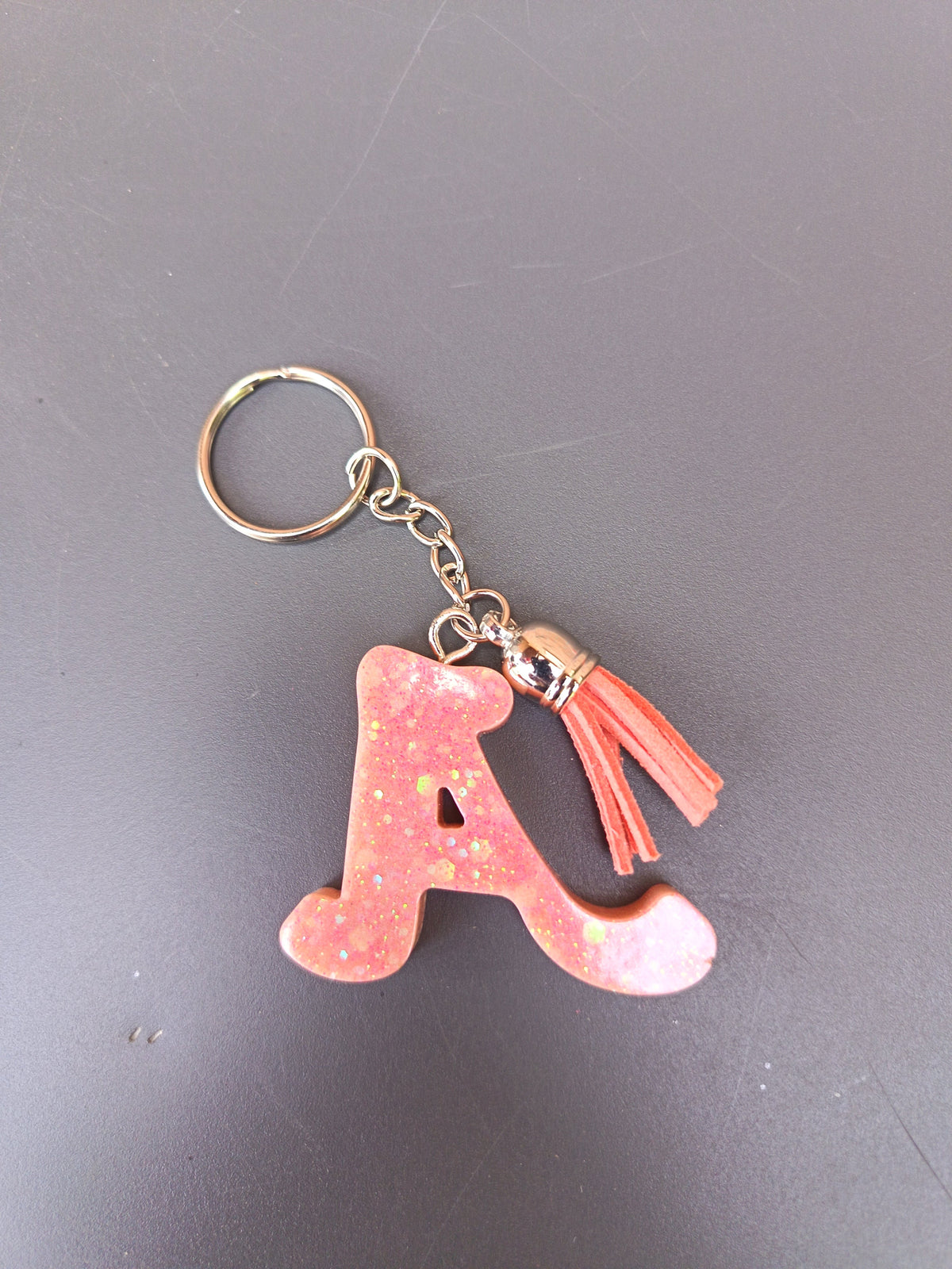 Porte-clé lettre A sculptée en résine rose pêche nacré à paillettes irisées avec pompon suédine rose saumon
