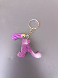 Porte-clé lettre A sculptée en résine violet fuchsia ultra-pailleté avec pompon suédine violet et anneau doré