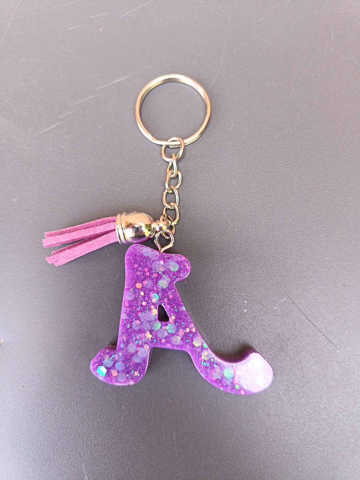 Porte-clé lettre A sculptée en résine violet améthyste à grosses paillettes holographiques irisées avec pompon suédine rose fuchsia et anneau doré