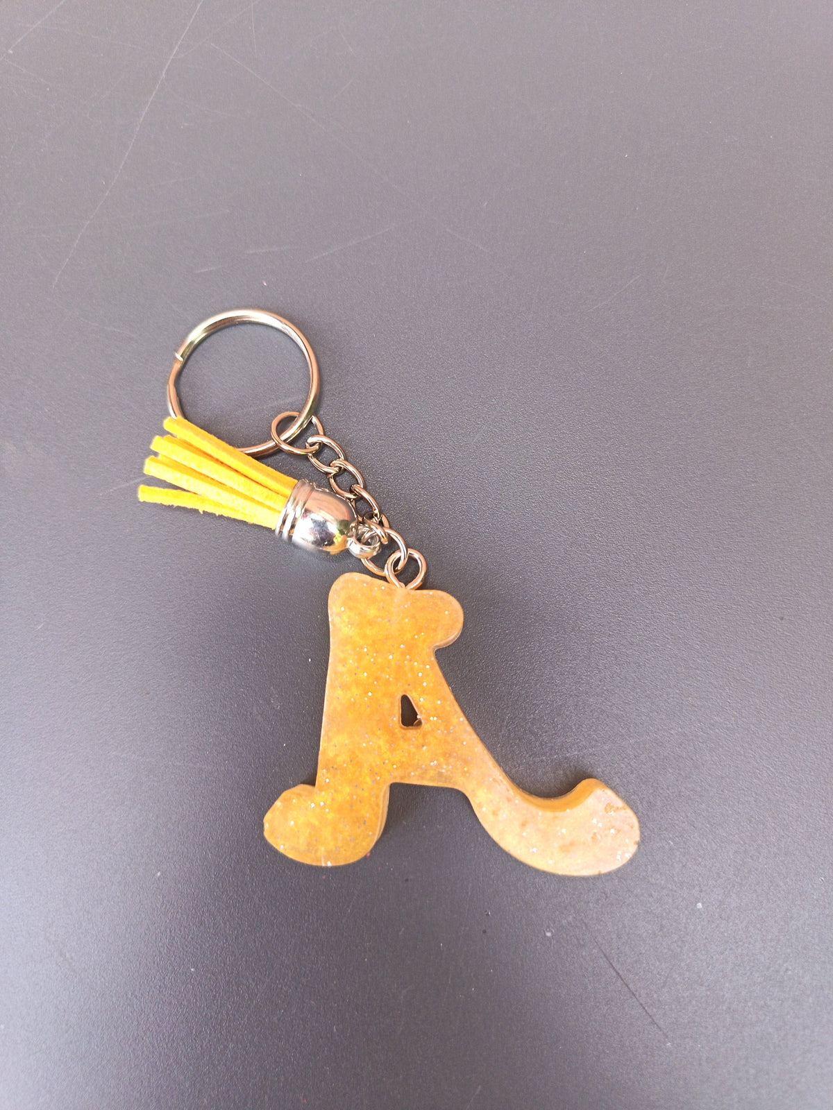 Porte-clé lettre A sculptée en résine ocre doré mat à micro-paillettes avec pompon suédine jaune vif et chaînette argentée