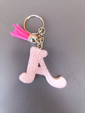 Porte-clé lettre A sculptée en résine rose poudré givré nacré avec pompon suédine rose fuchsia vif et anneau doré