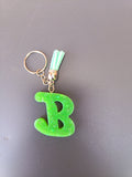 Porte-clé lettre B sculptée en résine vert anis fluo à paillettes holographiques avec pompon suédine vert menthe clair et chaînette dorée