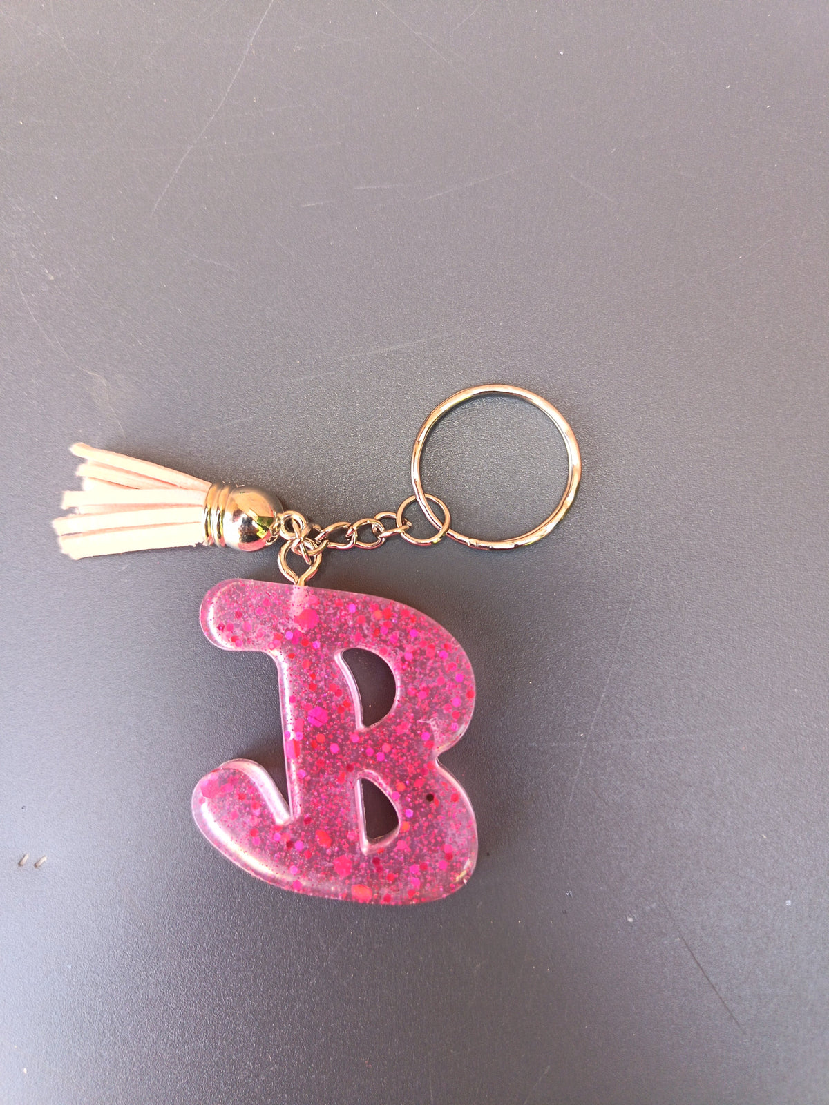 Porte-clé lettre B sculptée en résine rose fuchsia translucide à grosses paillettes holographiques avec pompon suédine blanc crème et chaînette dorée