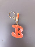 Porte-clé lettre B sculptée en résine orange terracotta à micro-paillettes cuivrées avec pompon suédine orange vif et chaînette argentée
