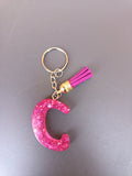 Porte-clé lettre C sculptée en résine rose fuchsia à grosses paillettes holographiques avec pompon suédine fuchsia et chaînette dorée