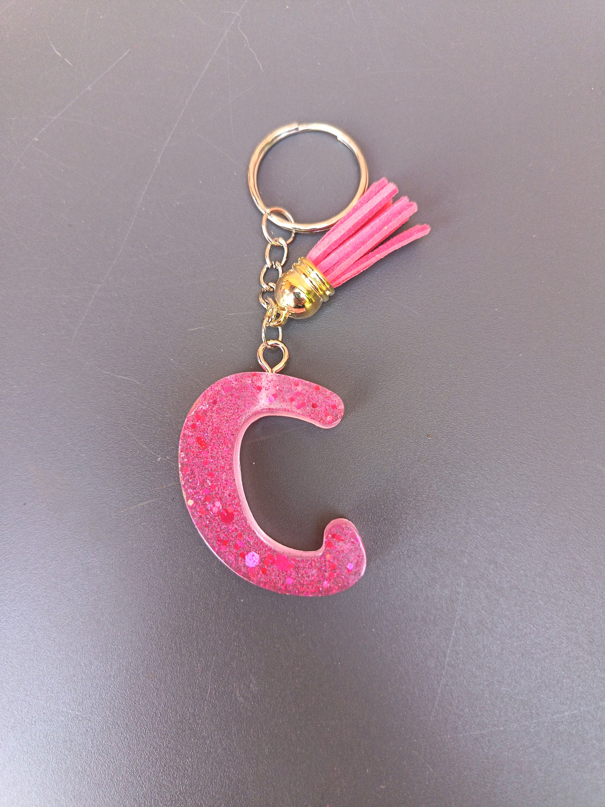 Porte-clé lettre C sculptée en résine rose bonbon translucide à grosses paillettes irisées avec pompon suédine rose vif et chaînette dorée