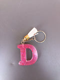 Porte-clé lettre D sculptée en résine rose fuchsia à grosses paillettes holographiques avec pompon suédine blanc crème et chaînette dorée