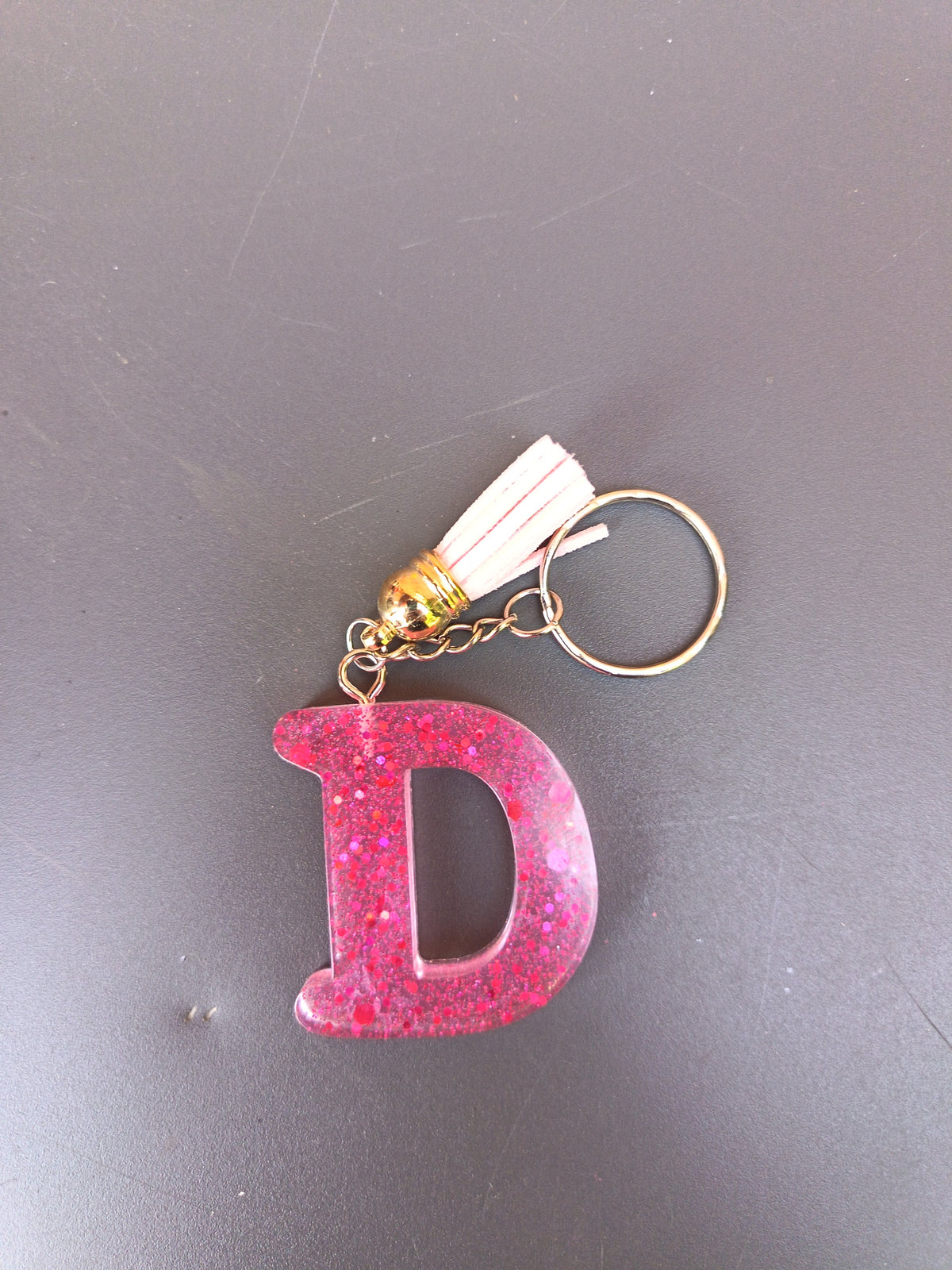 Porte-clé lettre D sculptée en résine rose fuchsia à grosses paillettes holographiques avec pompon suédine blanc crème et chaînette dorée