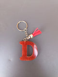 Porte-clé lettre D sculptée en résine rouge terracotta à micro-paillettes cuivrées avec pompon suédine rouge vif et chaînette argentée
