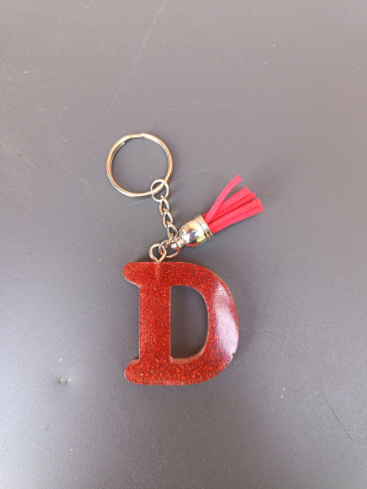 Porte-clé lettre D sculptée en résine rouge terracotta à micro-paillettes cuivrées avec pompon suédine rouge vif et chaînette argentée