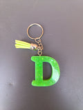 Porte-clé lettre D sculptée en résine vert fluo à grosses paillettes holographiques avec pompon suédine jaune fluo et chaînette argentée