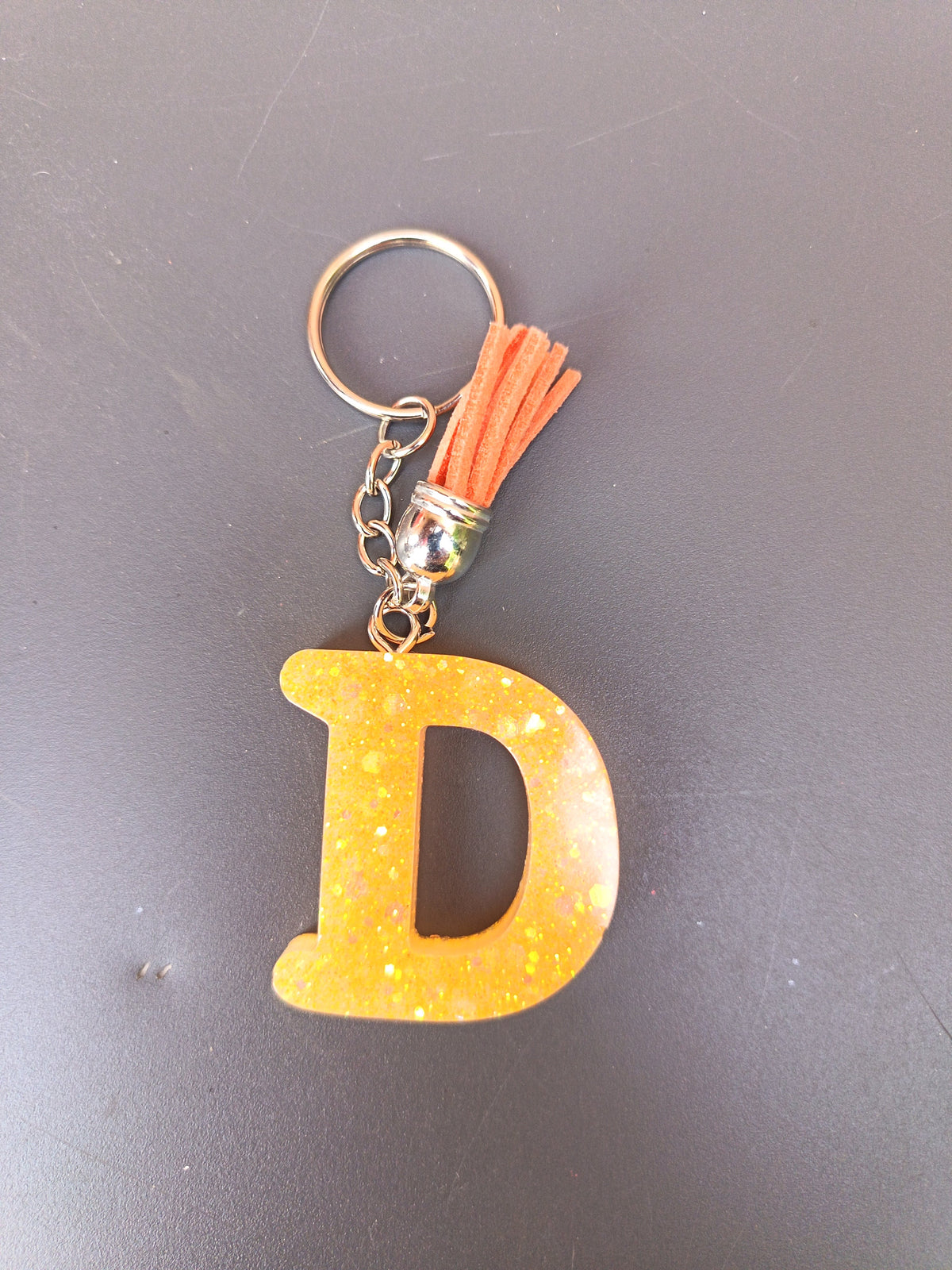 Porte-clé lettre D sculptée en résine jaune soleil à micro-paillettes dorées irisées avec pompon suédine orange saumon et chaînette argentée