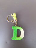Porte-clé lettre D sculptée en résine vert anis clair à micro-paillettes avec pompon suédine jaune fluo et chaînette argentée