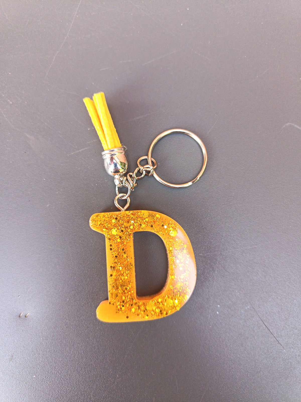 Porte-clé lettre D sculptée en résine orange doré translucide à grosses paillettes dorées avec pompon suédine jaune vif et chaînette argentée