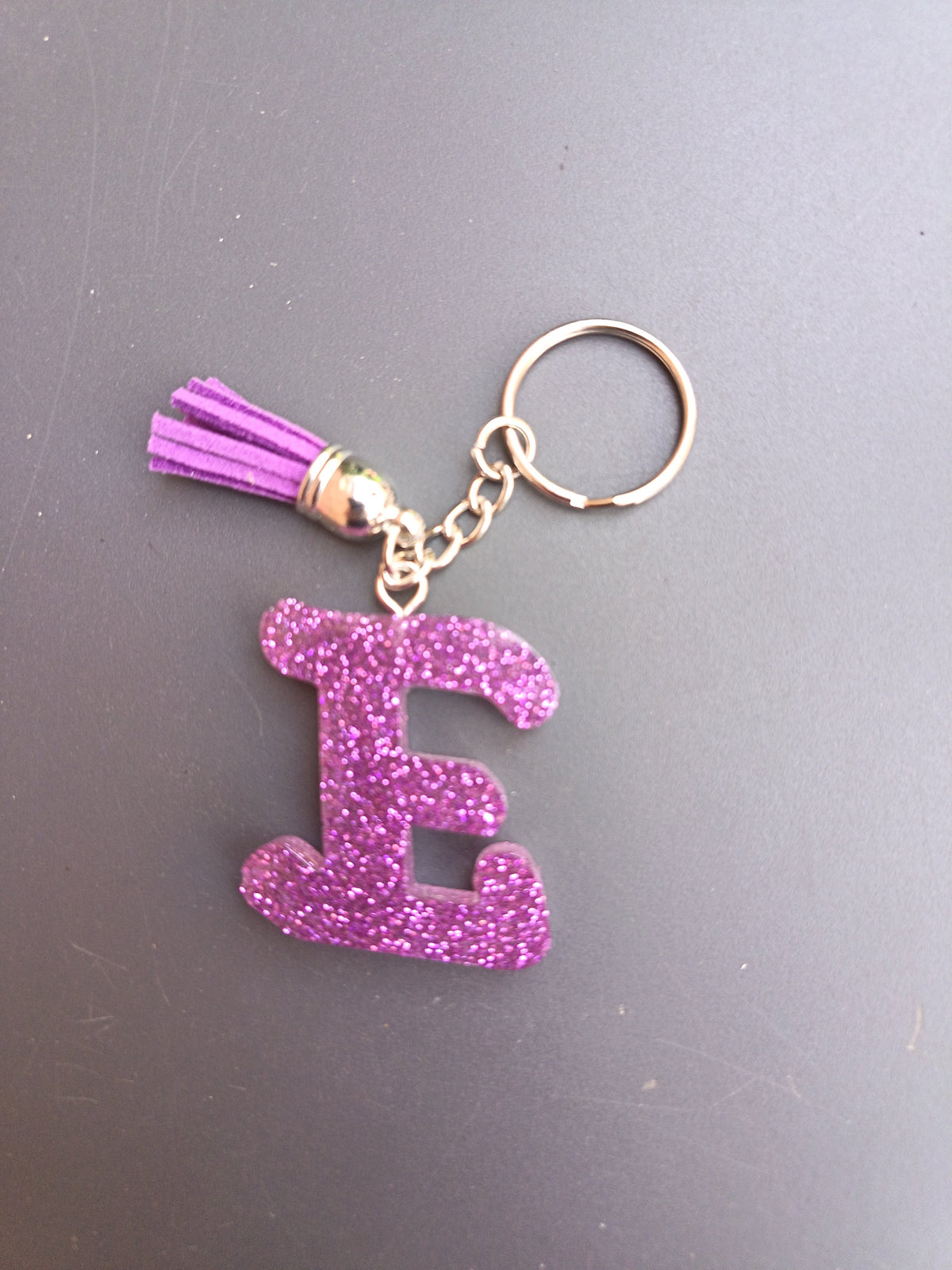 Porte-clé lettre E sculptée en résine violet fuchsia ultra-pailleté avec pompon suédine violet et chaînette argentée