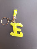 Porte-clé lettre E sculptée en résine jaune fluo à grosses paillettes irisées avec pompon suédine jaune fluo et chaînette argentée
