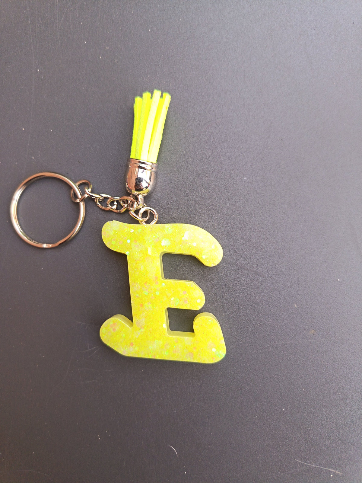 Porte-clé lettre E sculptée en résine jaune fluo à grosses paillettes irisées avec pompon suédine jaune fluo et chaînette argentée