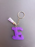 Porte-clé lettre E sculptée en résine violet améthyste mat à micro-paillettes avec pompon suédine lilas pastel et chaînette argentée